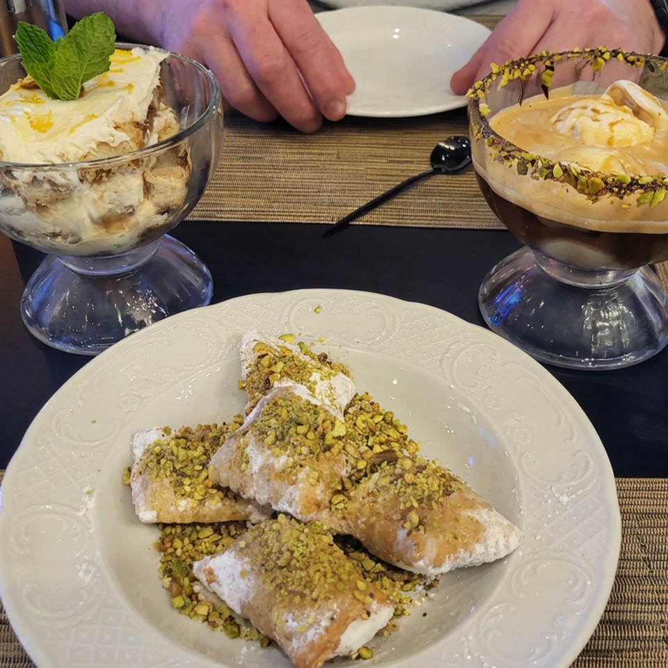 Pistachio-coated pastries sit on a plate beside two creamy desserts in glass dishes, one mint-garnished and one nut-rimmed.